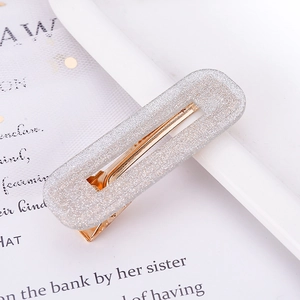 Detail of silver glitter acetate hair clip with golden metal base on a magazine page