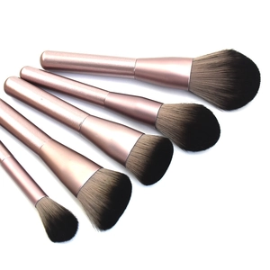 Close-up of five rose gold makeup brushes with soft gradient bristles on white background
