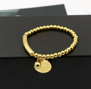 Detail of gold beaded bracelet with engraved coin charm and small sphere on black box