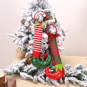 Christmas elf leg ornaments with bells and bows hanging on a snow-dusted tree