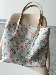 Close-up of floral pattern fabric tote bag with brown PU straps on a modern chair