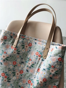 Close-up of floral canvas tote bag with leather handles and metal rivet details