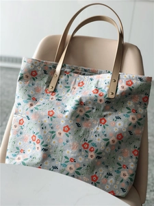 Detailed macro of floral canvas tote bag with brown leather handles and metal rivets