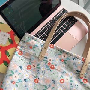 Close-up of floral canvas tote bag with brown leather handles and gold rivet details