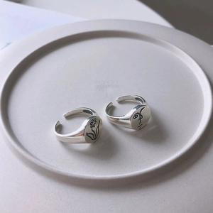 Detailed view of silver minimalist rings with engraved flower and face line art
