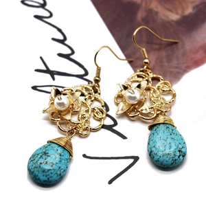 Detail of turquoise drop earrings with gold floral patterns and pearl accents on a magazine