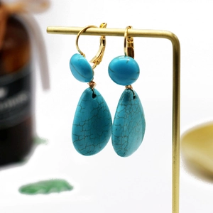 Detail view of bohemian turquoise drop earrings with gold plating on a display stand