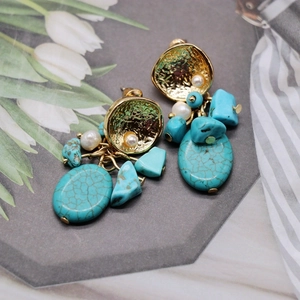 Detailed close-up of Bohemian earrings with turquoise stones and white pearls on gold metal