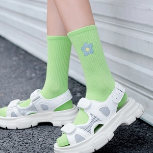 Green collegiate style mid-calf socks with blue flower embroidery worn with white sandals