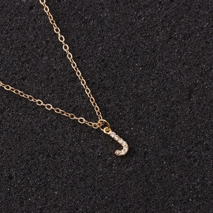 Detailed close-up of golden necklace featuring a crystal-encrusted letter J pendant