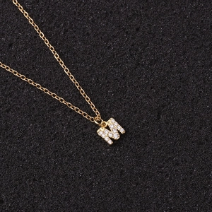 Detailed view of gold letter M pendant necklace with white zircon stones on a black pad