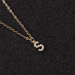Minimalist gold letter S pendant necklace with clear zircon stones on black background