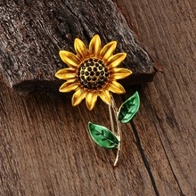 Detailed close-up of a golden sunflower brooch with black crystals on a rustic wood surface