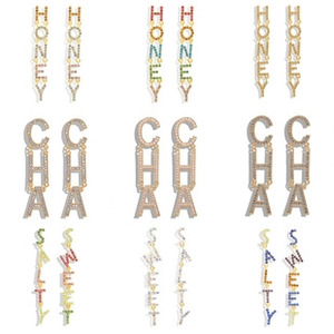 Macro shot of long drop earrings featuring crystal-encrusted letters in various colors