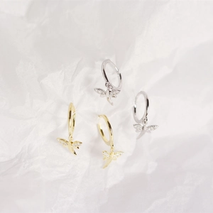 Detail of silver and gold dragonfly earrings with small diamonds on white paper background