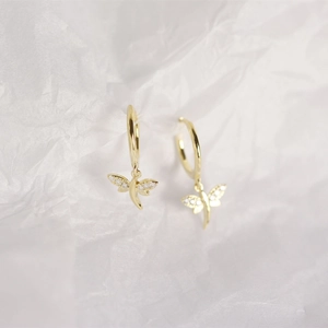 Macro shot of gold dragonfly earrings with sparkling white zircons on paper background