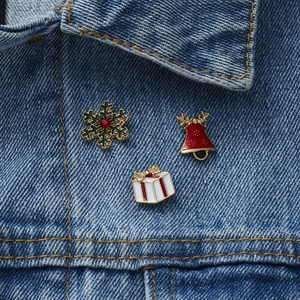 Detail of Christmas enamel pins set with snowflake, bell, and gift box on denim fabric