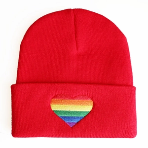 Close-up of vibrant red beanie featuring rainbow striped heart embroidery on folded brim