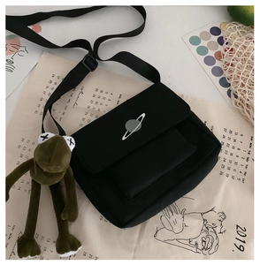 Detail of black canvas messenger bag featuring planet embroidery and frog plush charm