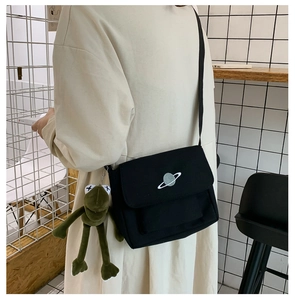 Detail of black canvas crossbody bag with planet embroidery and green frog charm on a model