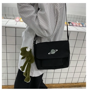 Detail of black canvas messenger bag featuring a planet logo and green frog plush charm