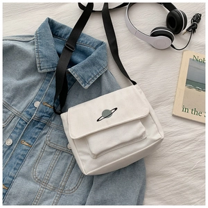 Detailed close-up of white canvas crossbody bag with planet embroidery and black strap