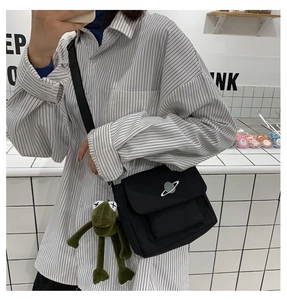 Detail of black canvas crossbody bag with planet embroidery and green frog pendant