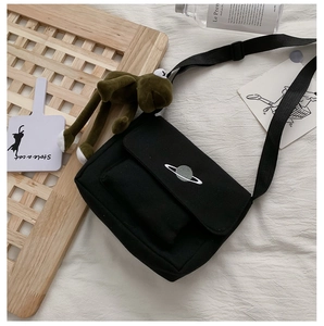 Detail of black canvas crossbody bag with planet embroidery and green frog plush charm