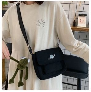 Detail of black canvas crossbody bag with planet embroidery and green plush frog charm