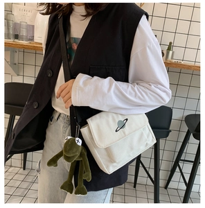 Close-up of white canvas messenger bag with planet embroidery and green frog charm