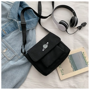 Close-up of black canvas crossbody bag with planet embroidery on white textured linen
