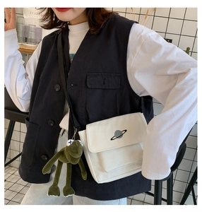 Detail of white canvas crossbody bag with planet embroidery and green plush frog charm