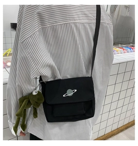 Detail of a black canvas crossbody bag with planet embroidery and a green frog plush toy