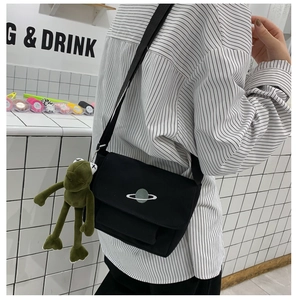 Detail of minimalist black canvas messenger bag featuring a planet embroidery and frog plush charm