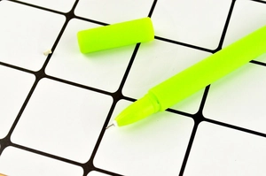 Close-up of a matte green clover leaf gel pen with the cap removed on a grid background