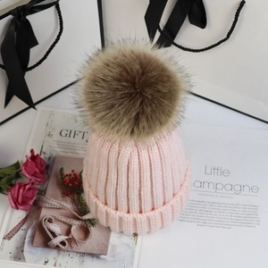 Rosa Strickmütze mit großem Kunstfell-Bommel auf dekorativem Geschenkhintergrund