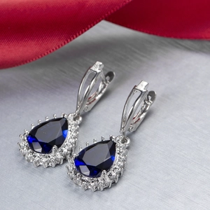 Macro shot of blue pear-shaped zircon earrings with silver prong setting and diamond halo