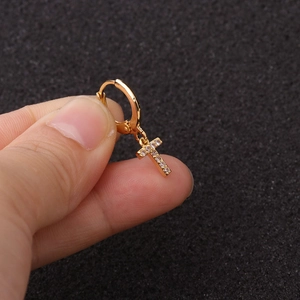 Détail d'une boucle d'oreille créole dorée avec un petit pendentif croix serti de zircons