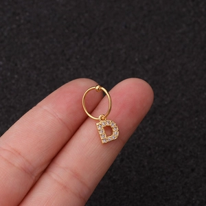 Détail d'une boucle d'oreille dorée lettre D avec zircons tenue sur un doigt