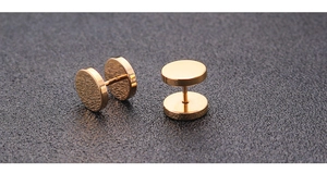 Macro detail of gold barbell stud earring with dual-sided circular design on black background