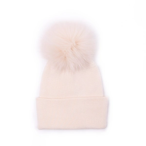 Detail of cream rib-knit baby hat with large faux fur pom-pom on white background