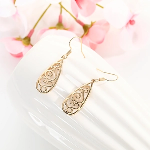 Detailed view of gold hollow teardrop earrings with Celtic swirl patterns on ceramic
