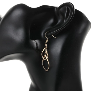 Detailed view of gold twisted dangling earrings worn on a black jewelry display model