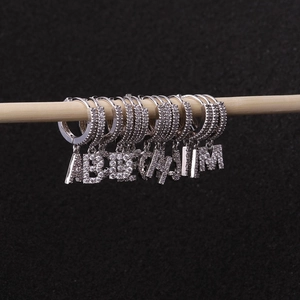 Silver alphabet hoop earrings with cubic zirconia charms hanging on a light wooden rod