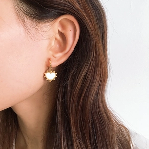 Close-up of heart-shaped gold earring with white shell inlay worn by a model