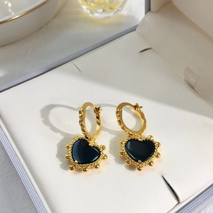 Elegant gold earrings featuring black heart charms with golden bead edges on jewelry box