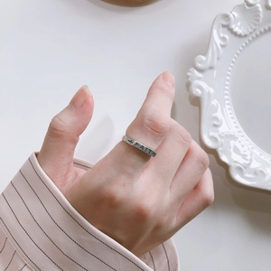 Detail shot of silver FAITH cross ring on finger with elegant ceramic plate background