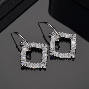 Elegant geometric square silver earrings with baguette-cut zircons on a reflective surface