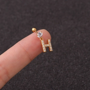 Macro view of a gold-plated letter H earring with zircon stones held on a finger