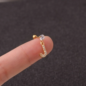 Macro shot of gold letter J charm earring with zircon stone inlay held by fingers